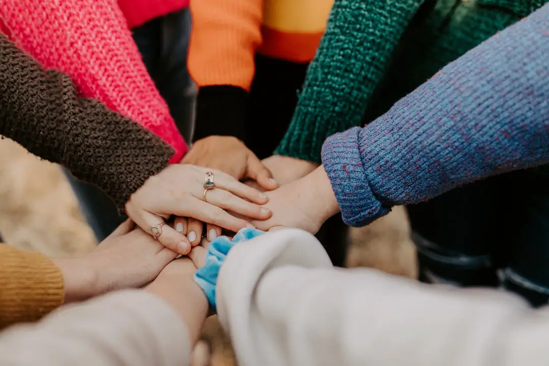 Girl friends hands piled togethger by Community Gardening person in red sweater holding babys hand